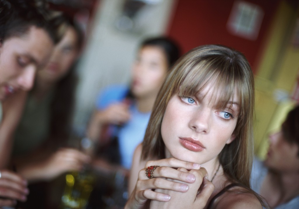 Teenage Girl Sitting in a Cafe Looking Bored and Lonely, Her Friends in the Background