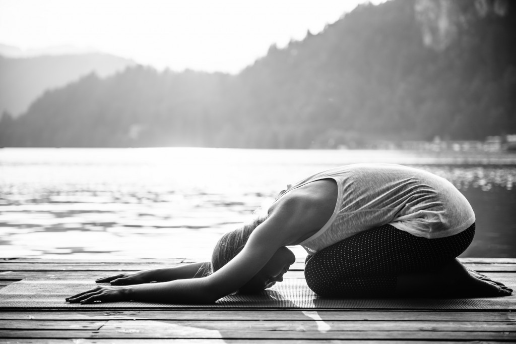 Young woman doing yoga by the lake, childs pose