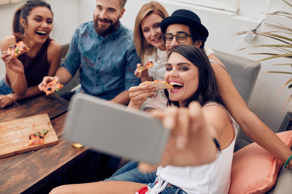 Young people taking a selfie while eating pizza